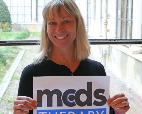 Dr. Melita Irving smiling holding a MCDS Therapy sign